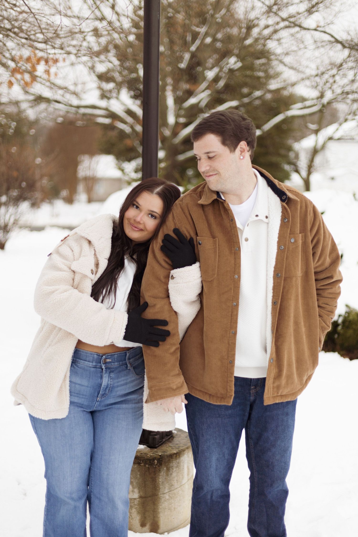 Cozy winter portrait of couple in warm jackets standing by lamp post in snow.