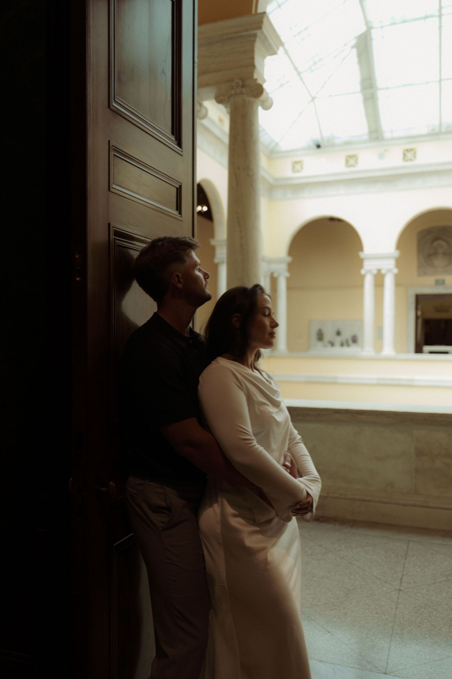 A series of black and white photos showing two people embracing in an elegant indoor space with arched windows and columns.