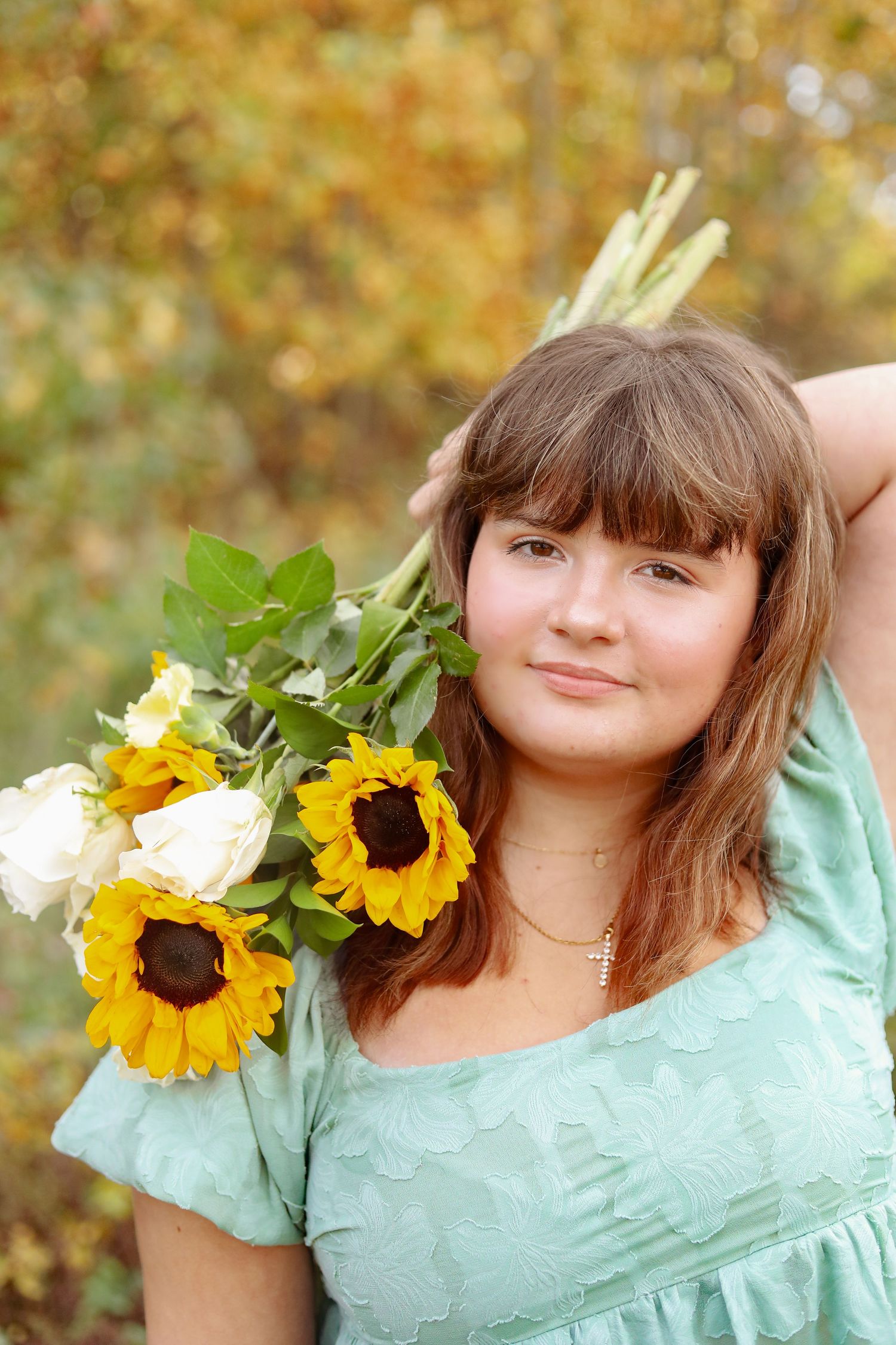 Person in mint dress holds sunflowers in autumn outdoor setting.