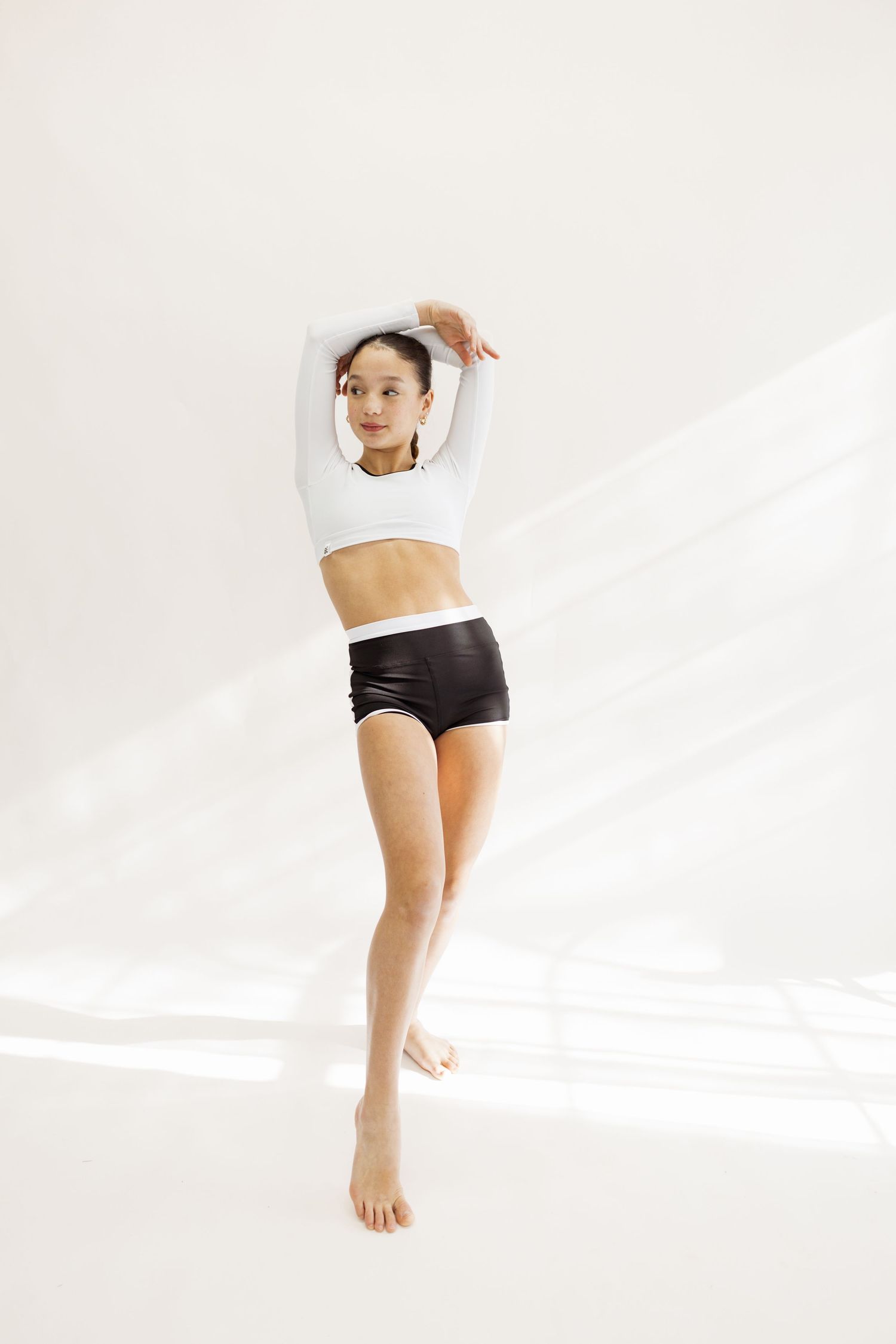 Dancer in white crop top and black shorts performs graceful movement in minimalist studio.