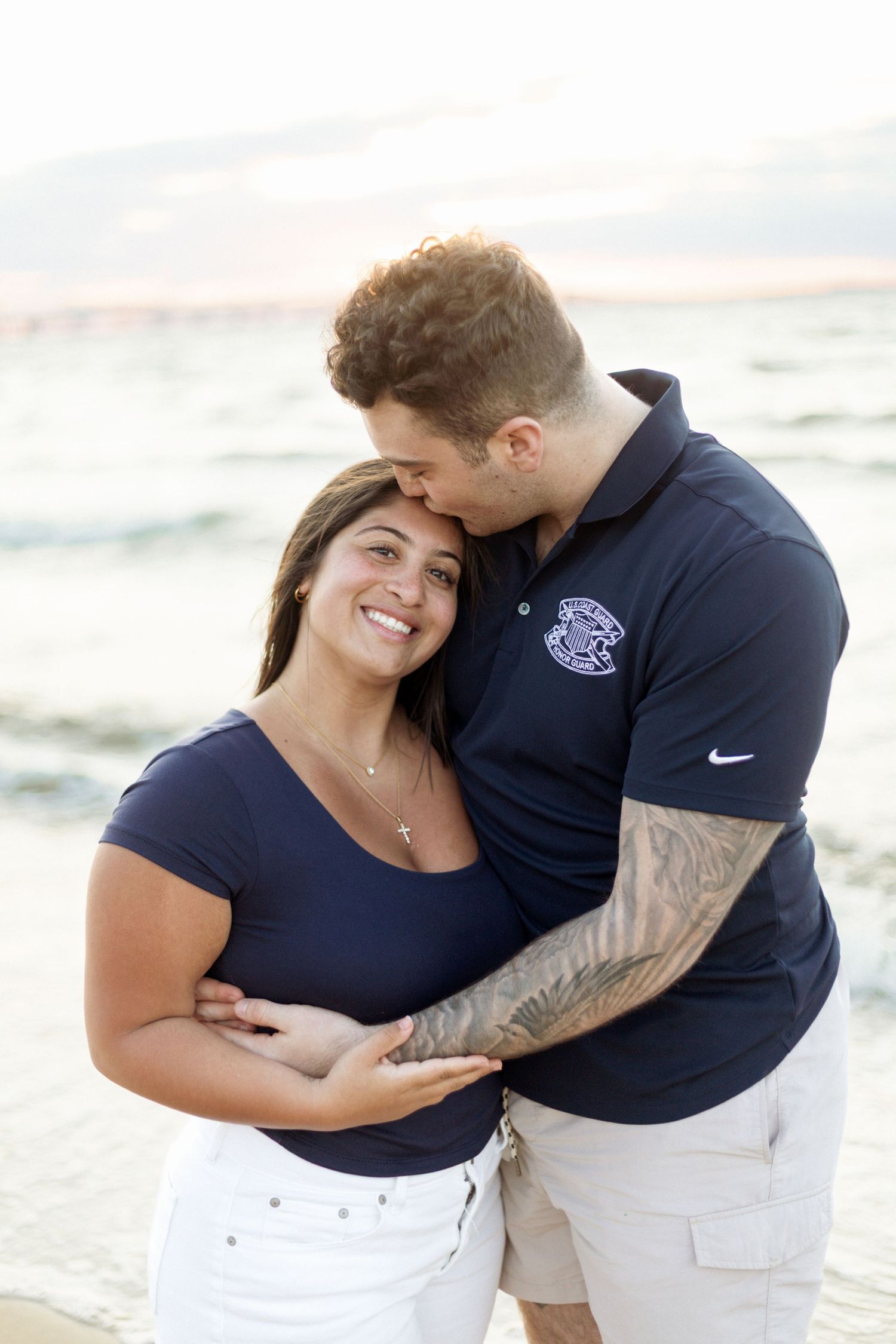 Romantic couple embracing on beach at sunset wearing matching navy outfits.