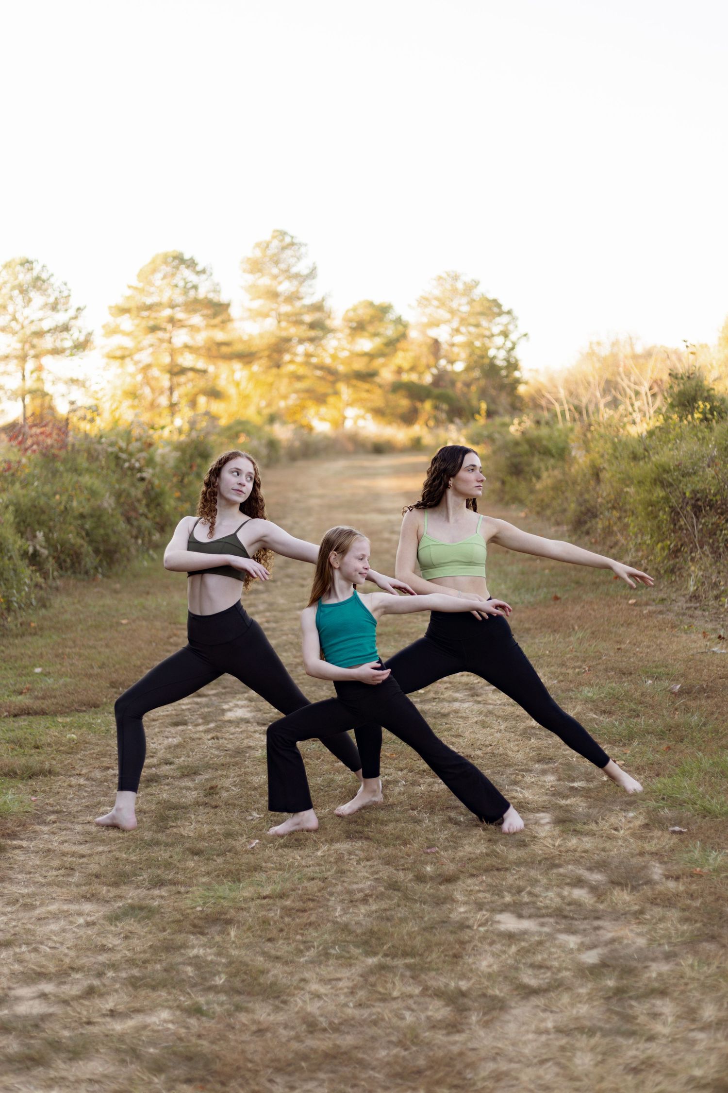 Dancers strike warrior pose in formation on nature trail at sunset.