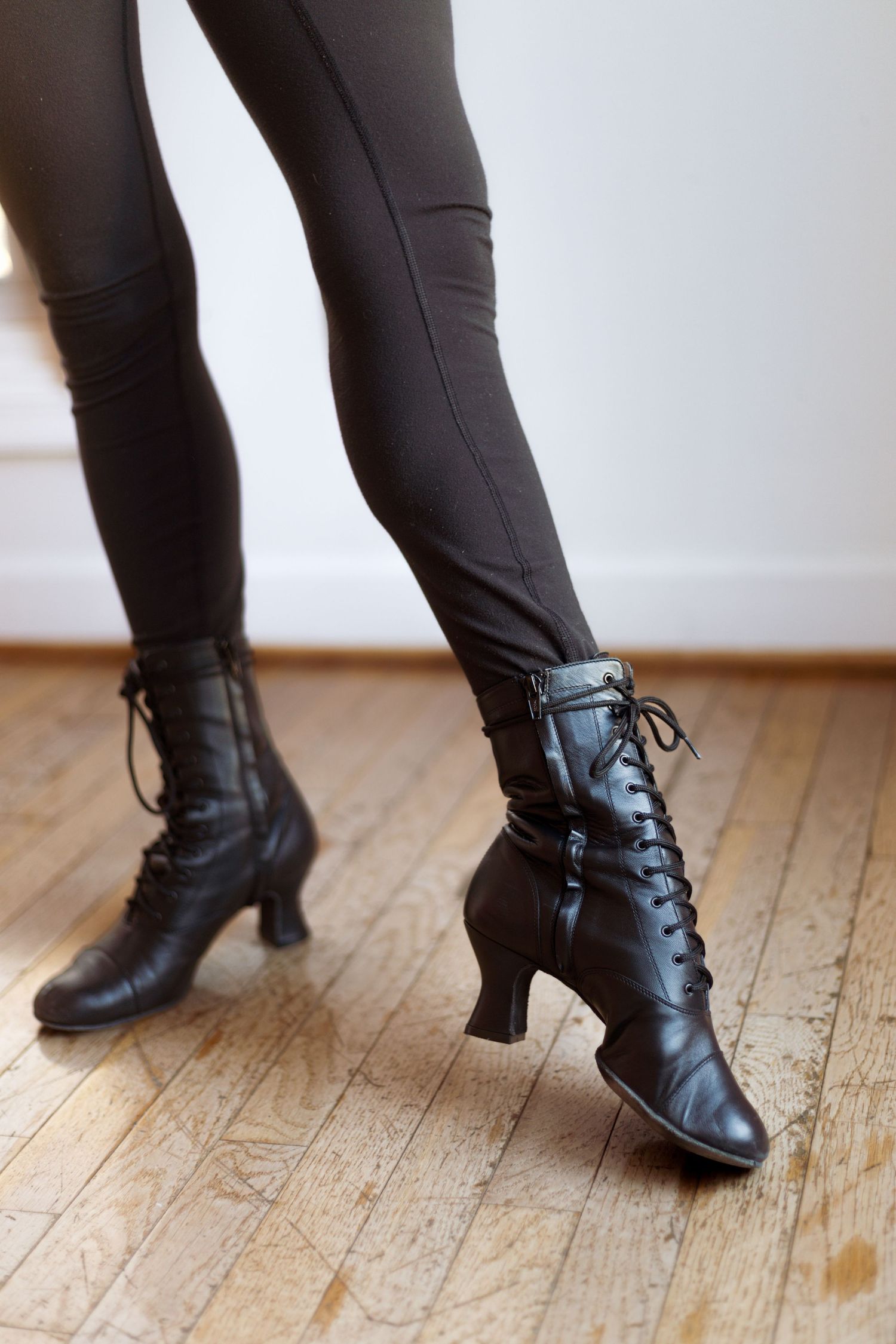 Close-up of vintage black lace-up dance boots with heels on wooden floor.