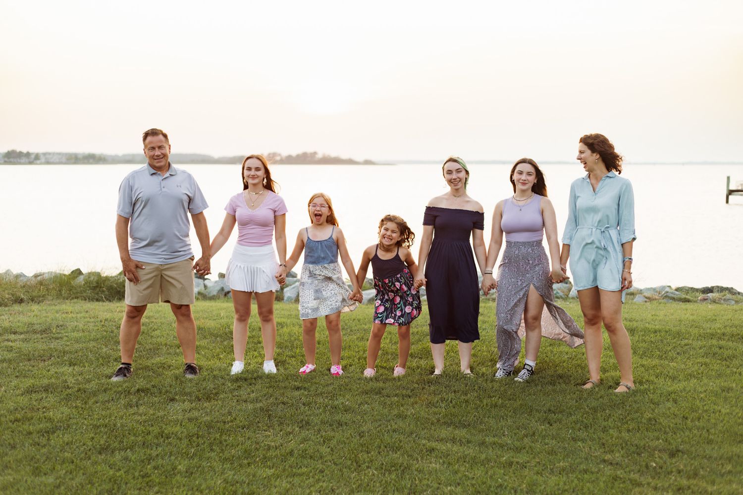 Family of seven walking hand in hand along waterfront path at dusk.