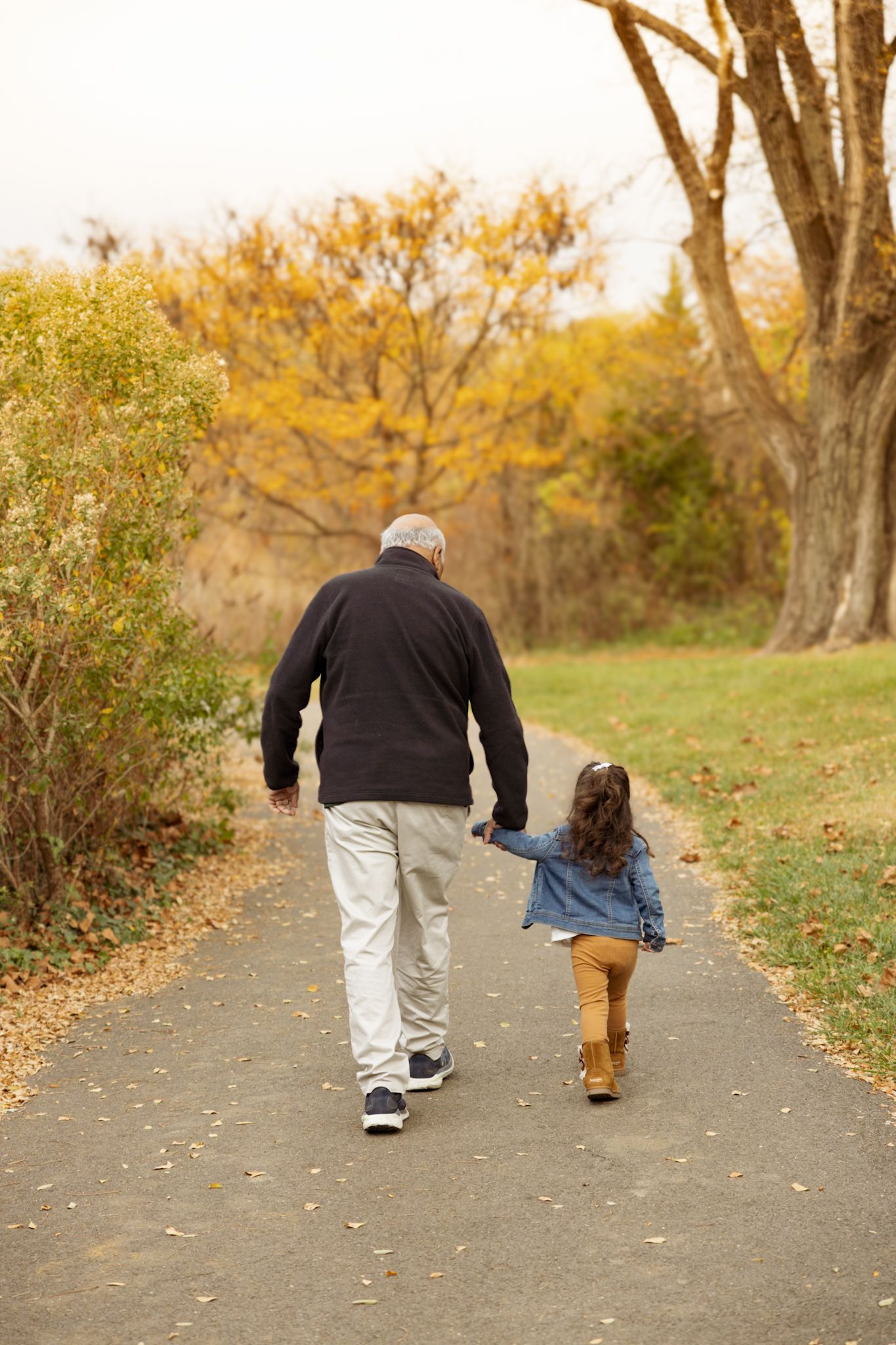 Adult and child walking together on autumn path surrounded by fall foliage.