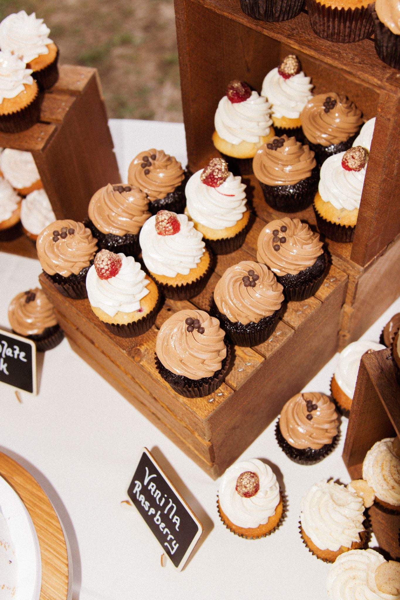 Elegant wooden tiered cupcake display with chocolate and vanilla frosted cupcakes topped with raspberries and chocolate chips.