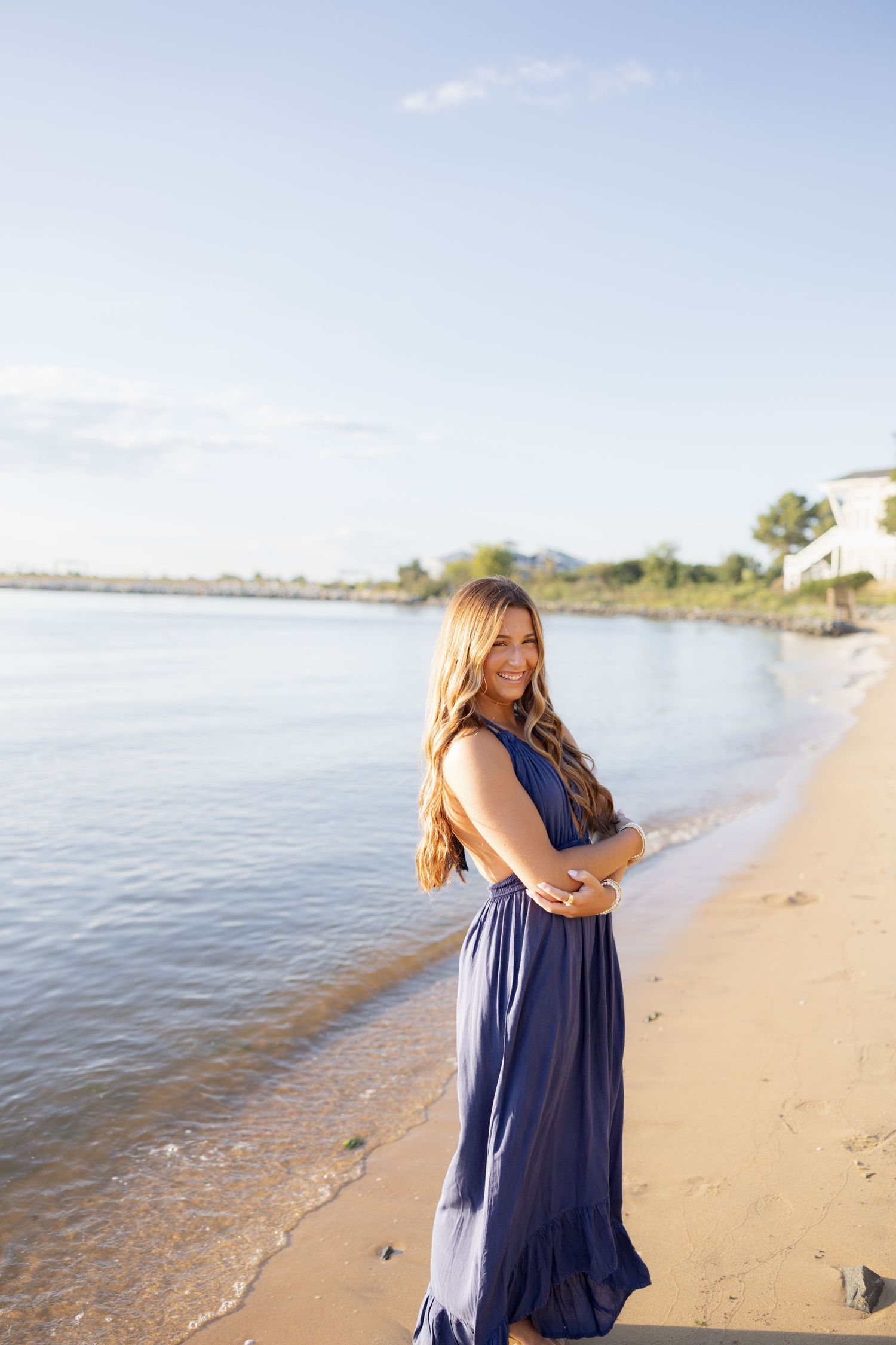 A person in a navy blue dress walks along a sandy beach shoreline at sunset.