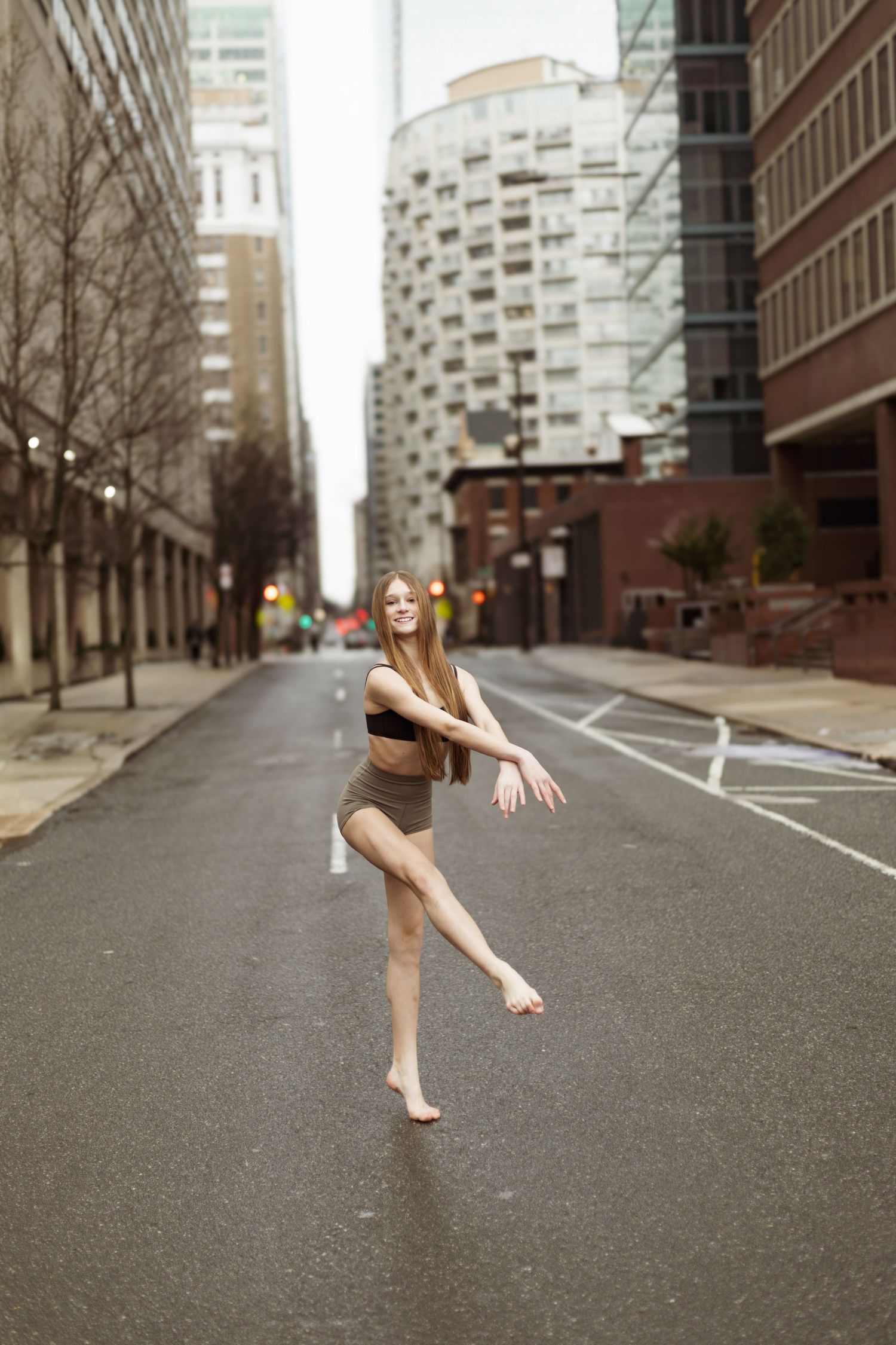 Dancer performs graceful pose on empty urban street with modern buildings.