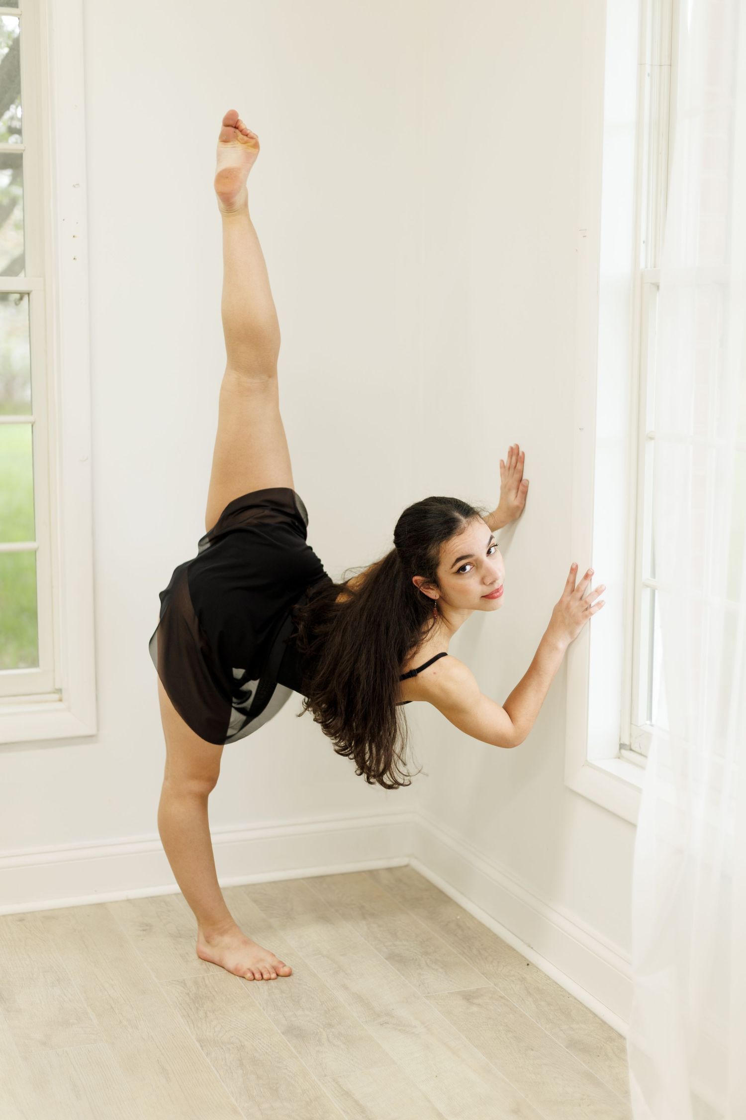 Dancer performs high leg extension against white wall in modern dance studio.