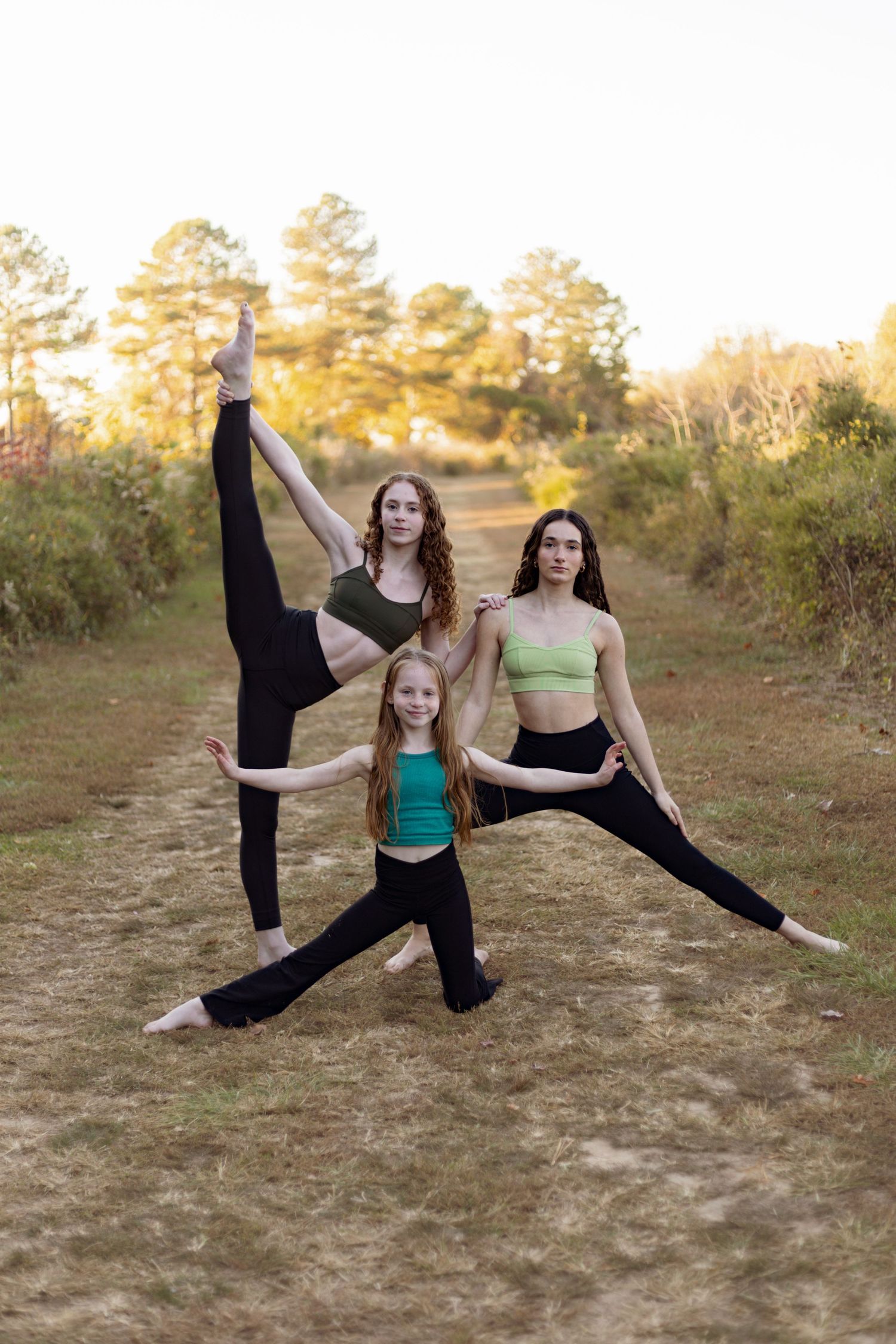 Three dancers strike synchronized poses on outdoor trail at golden hour.