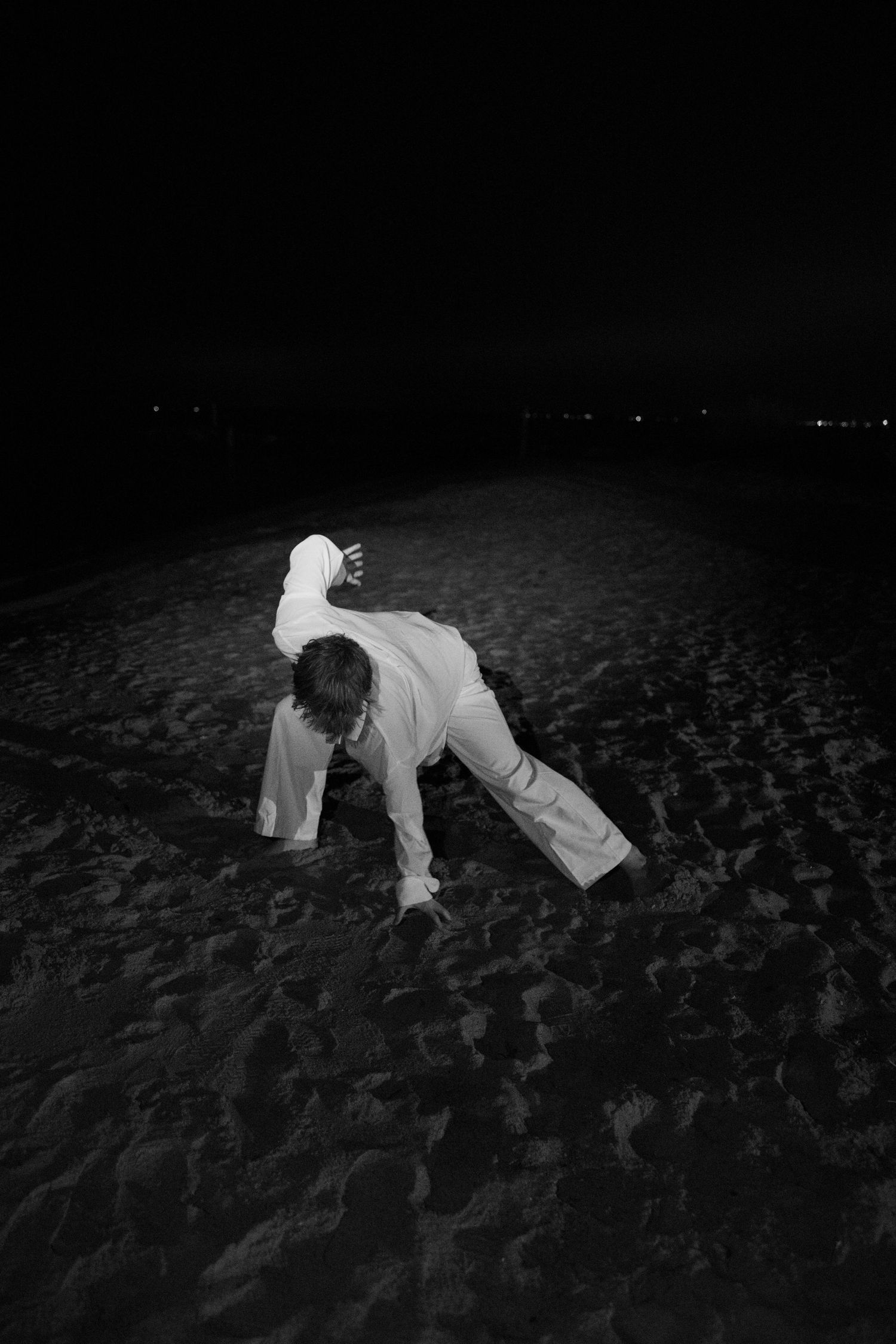 A sequence of black and white photos showing a person in white clothing falling onto a dark sandy beach at night.