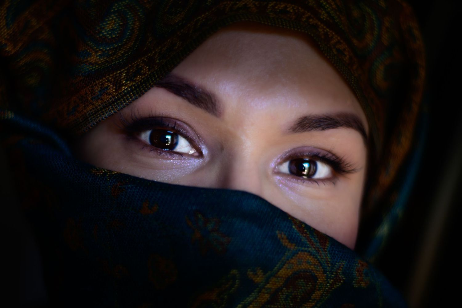Close-up portrait of woman with expressive eyes wearing decorative teal hijab headscarf.