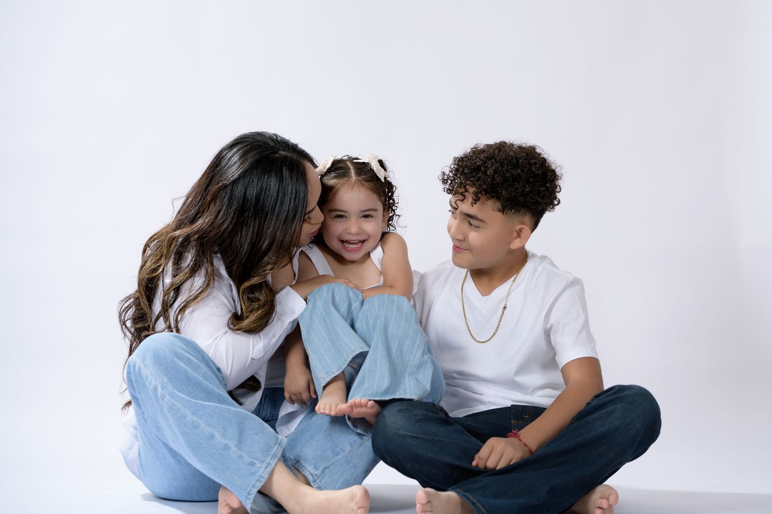 A woman and two children sit together on a white background, smiling and sharing a joyful family moment.