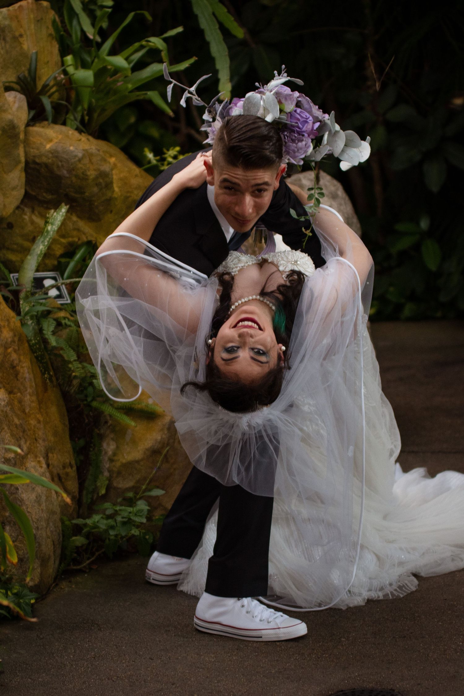 Groom dipping bride in white wedding dress and Converse sneakers during fun outdoor wedding photo.