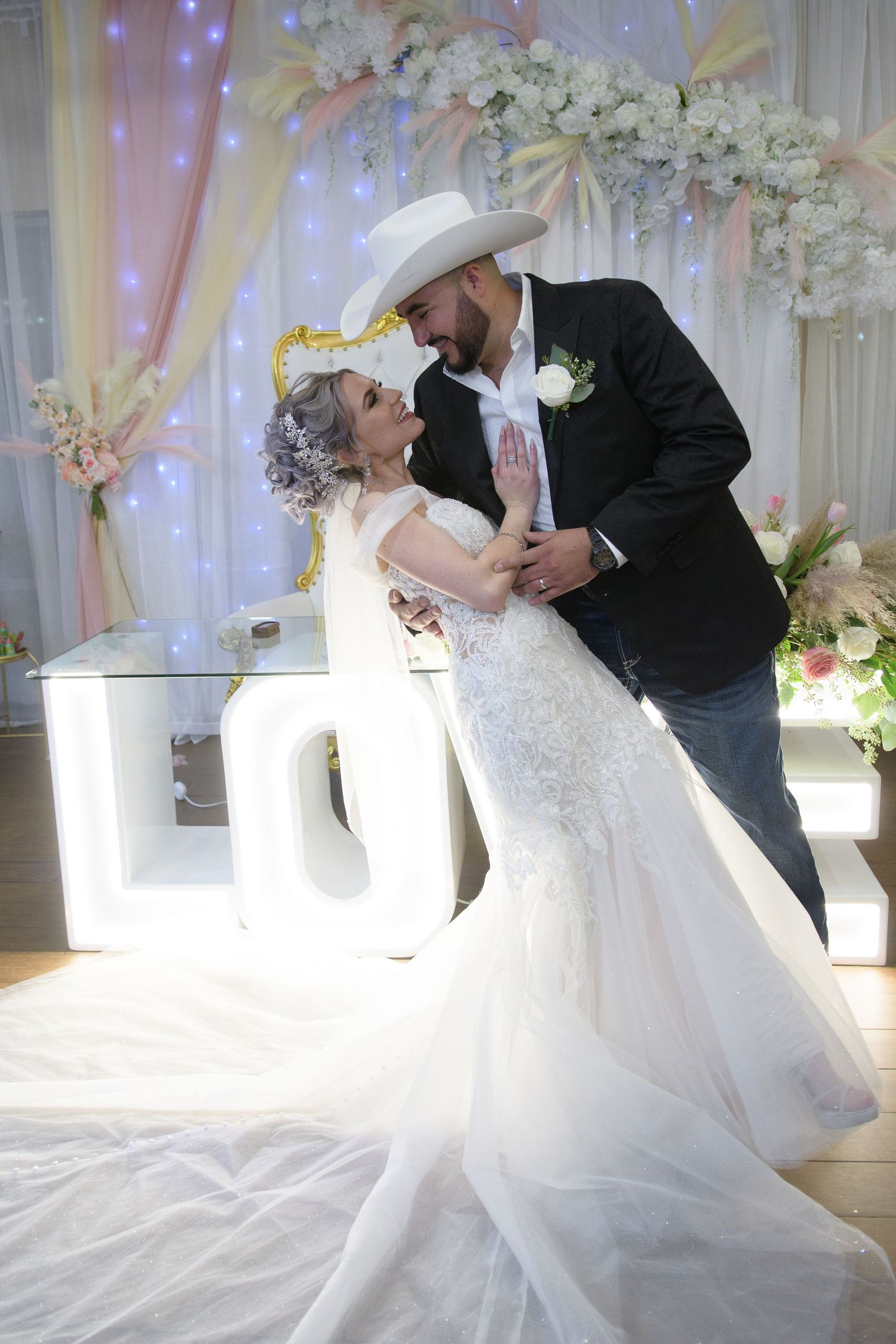 Bride and groom dancing at wedding reception with floral arch and illuminated LOVE letters backdrop.