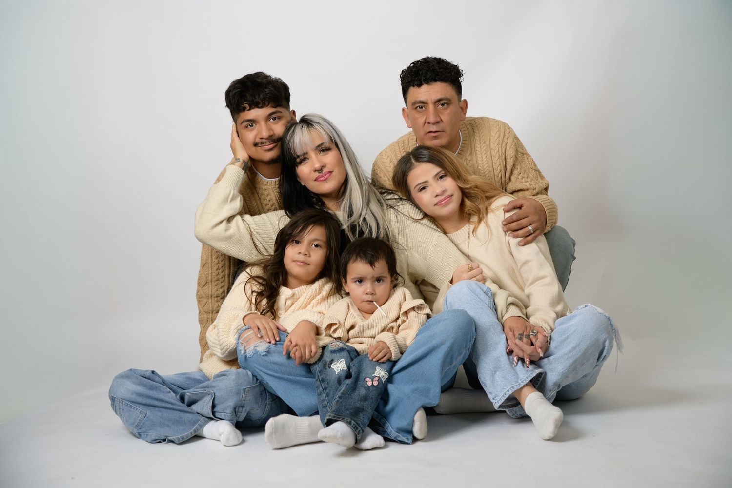 Happy family of six posing together in matching beige outfits with three young children in studio.