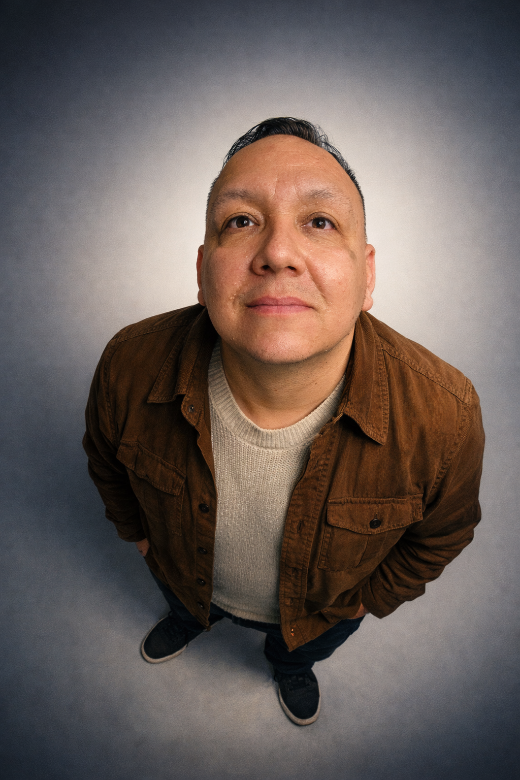 A man in a brown corduroy jacket and cream sweater photographed from above against a gray background.