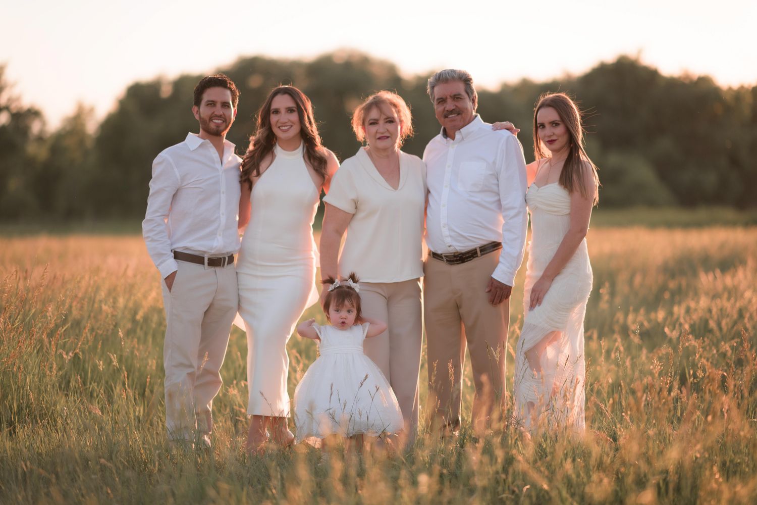 Multi-generational family in white outfits posing together in a golden sunlit field during sunset.