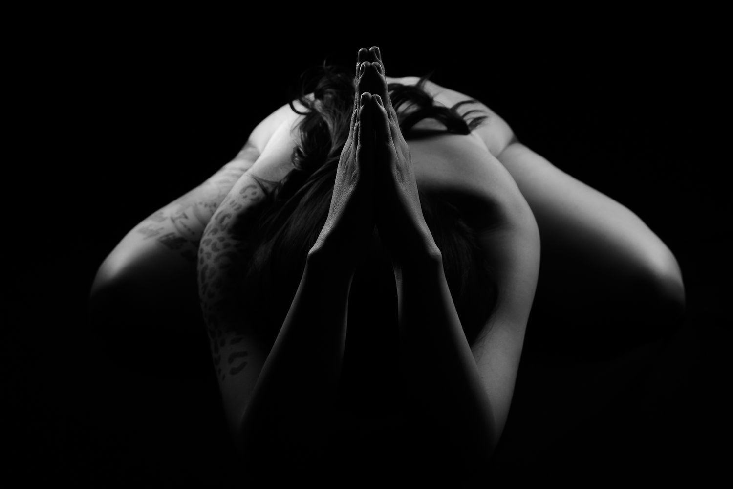 Artistic black and white photo of tattooed person with hands pressed together in prayer pose.
