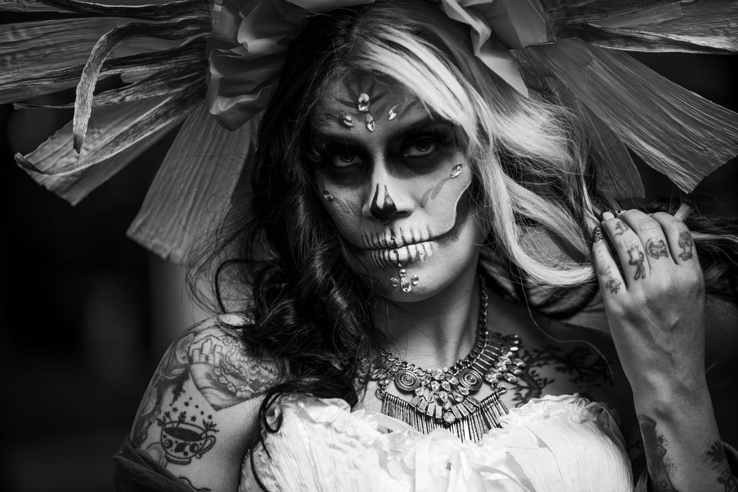 Black and white portrait of woman with Day of the Dead sugar skull makeup and large floral headpiece.