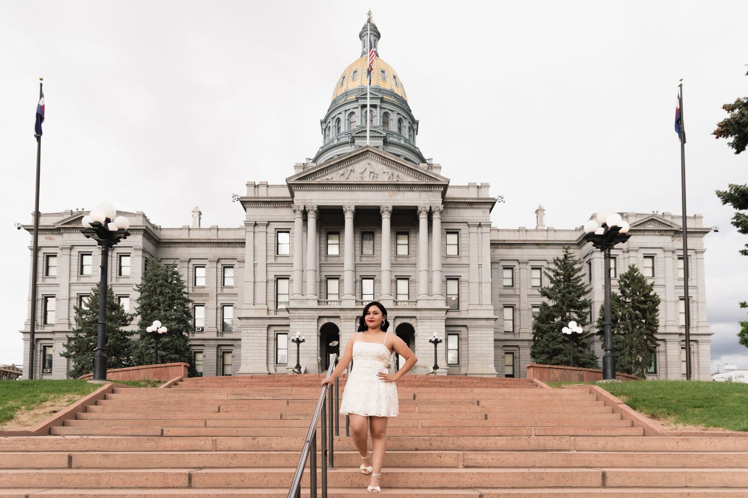 Young woman in white dress standing on steps in front of a grand capitol building with golden dome.