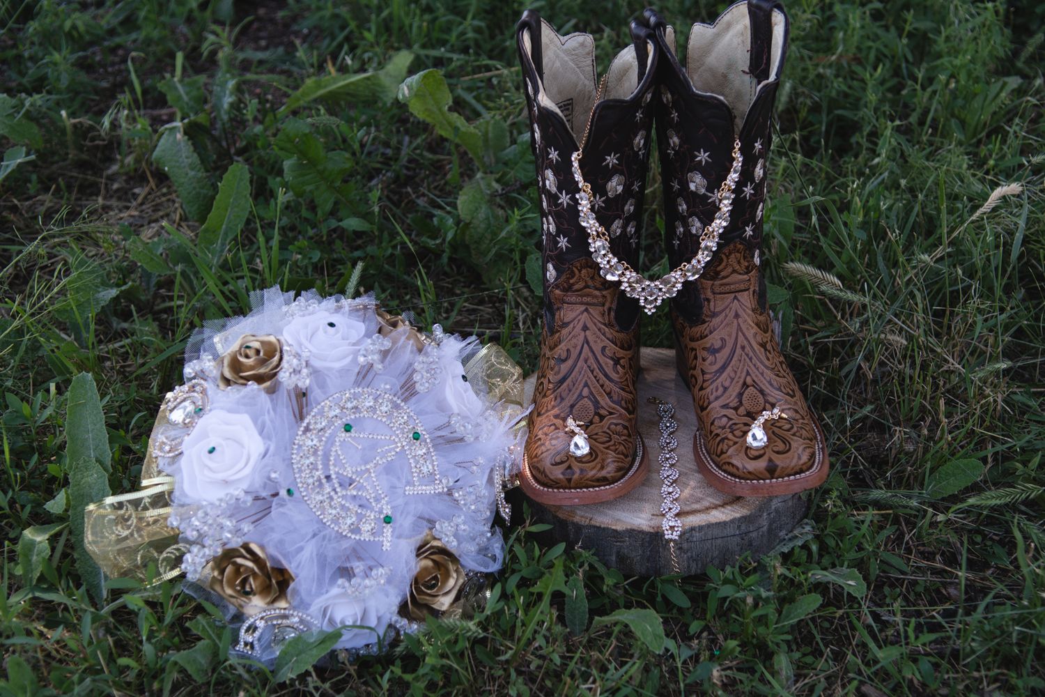 Decorative white and gold floral bouquet beside embellished brown cowboy boots on green grass.
