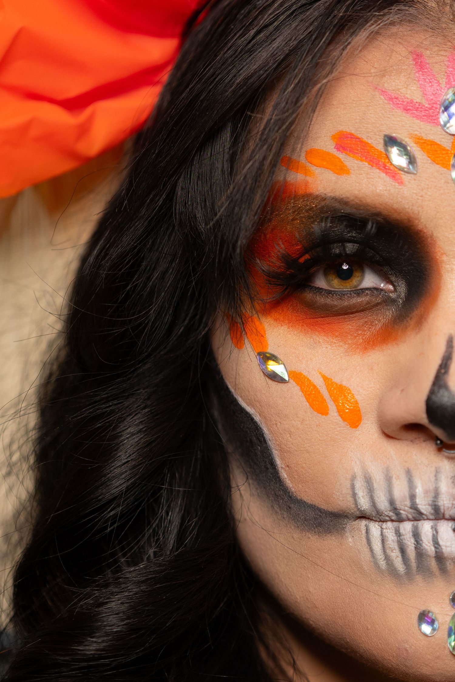 Close-up of woman with vibrant Day of the Dead sugar skull makeup and orange floral headpiece.