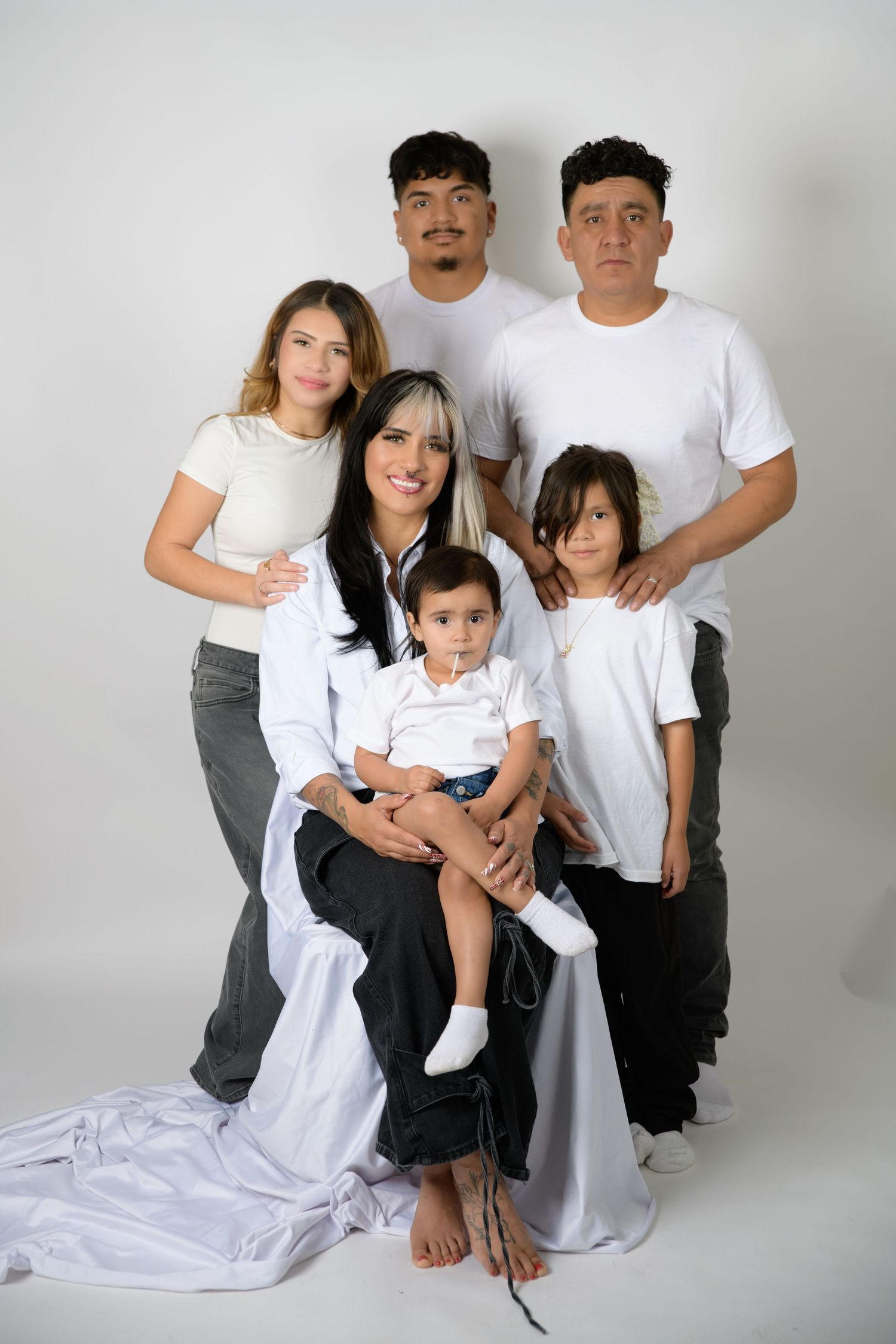 Family of six posing together in white tops and dark pants against a white studio background.