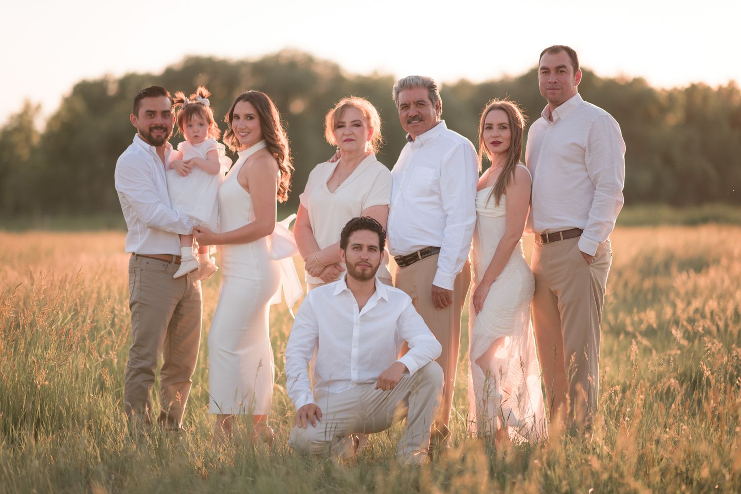 Family portrait in white outfits posing in golden field at sunset.