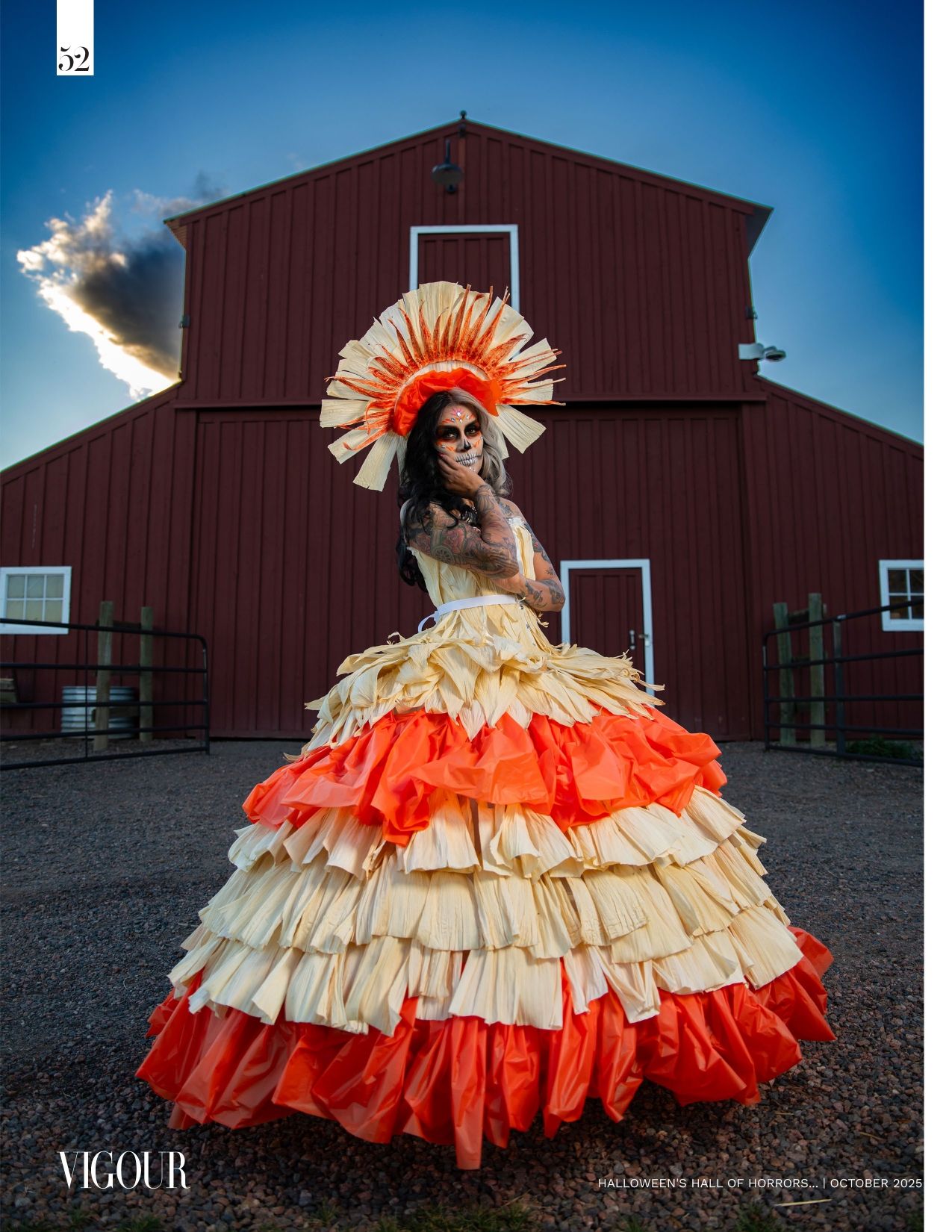 Woman in a tiered orange and cream ruffled gown and sunburst headdress poses with skull makeup before a red barn at sunset.