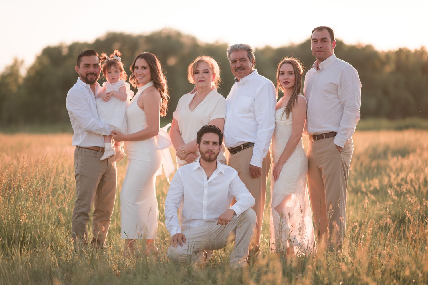 Large family group poses together in coordinating white outfits during golden hour in open field.