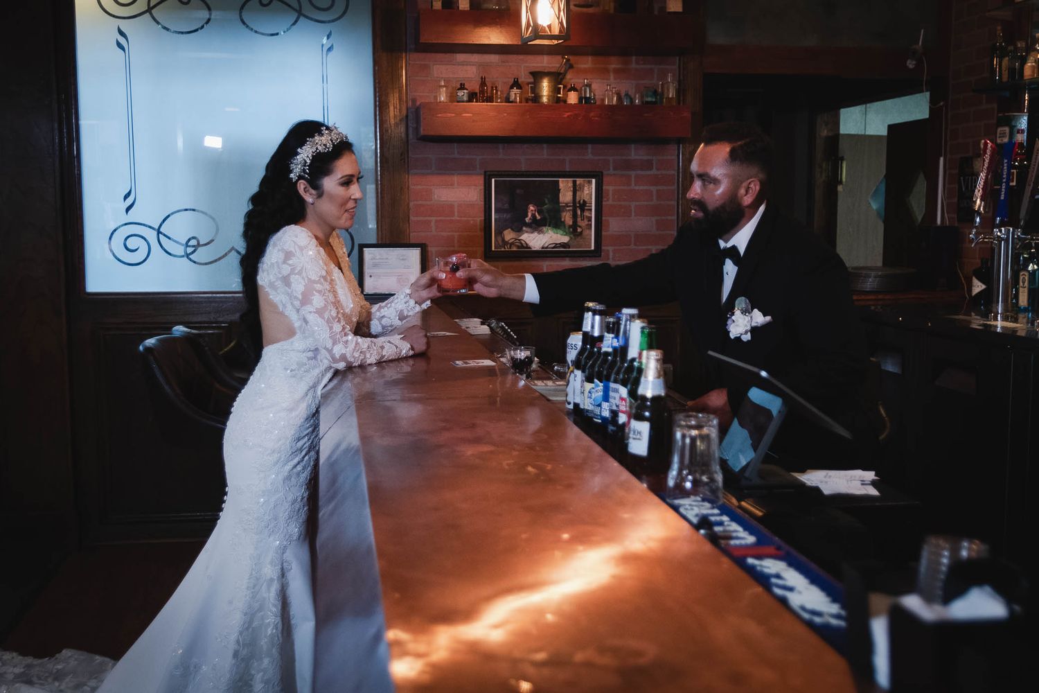 Bride and groom share a romantic moment at a warmly lit wooden bar on their wedding day.