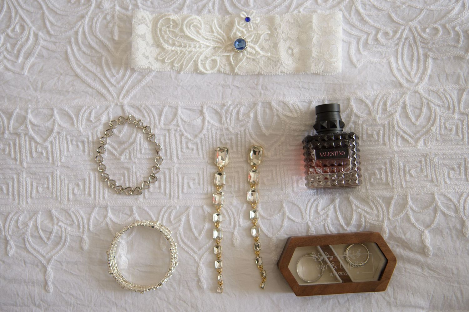 Flat lay of bridal accessories including garter, gold jewelry, perfume bottle, and wedding details.