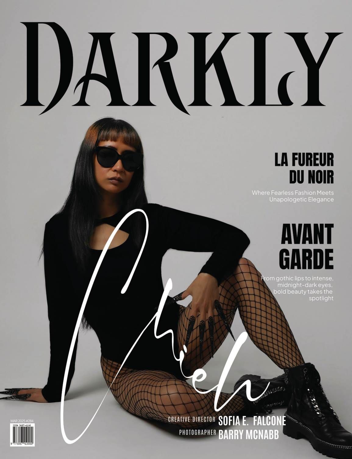 Darkly magazine cover with a model in black bodysuit, fishnet tights, sunglasses and combat boots posing on a gray backdrop.