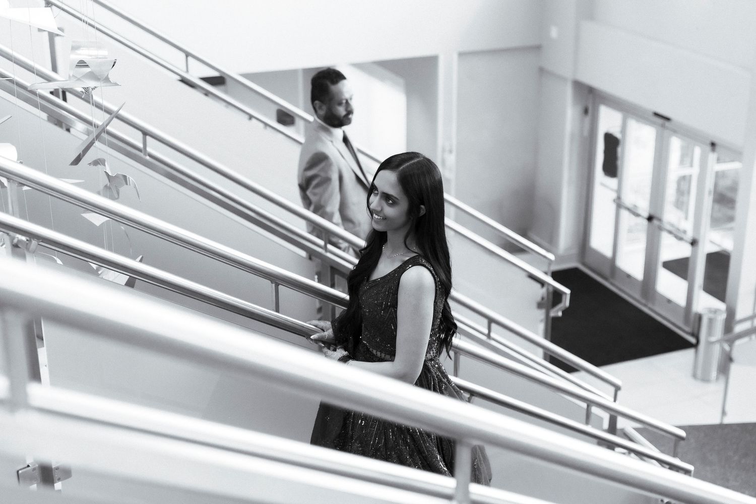 Black and white photo of a man and woman walking down stairs in a modern building with metal railings.