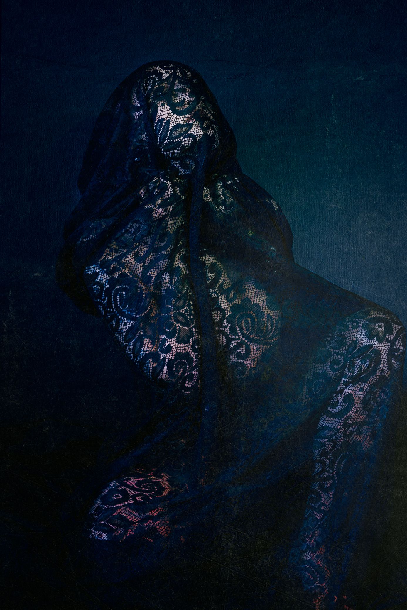 A mysterious figure wrapped in dark floral lace veil against a deep blue textured background.