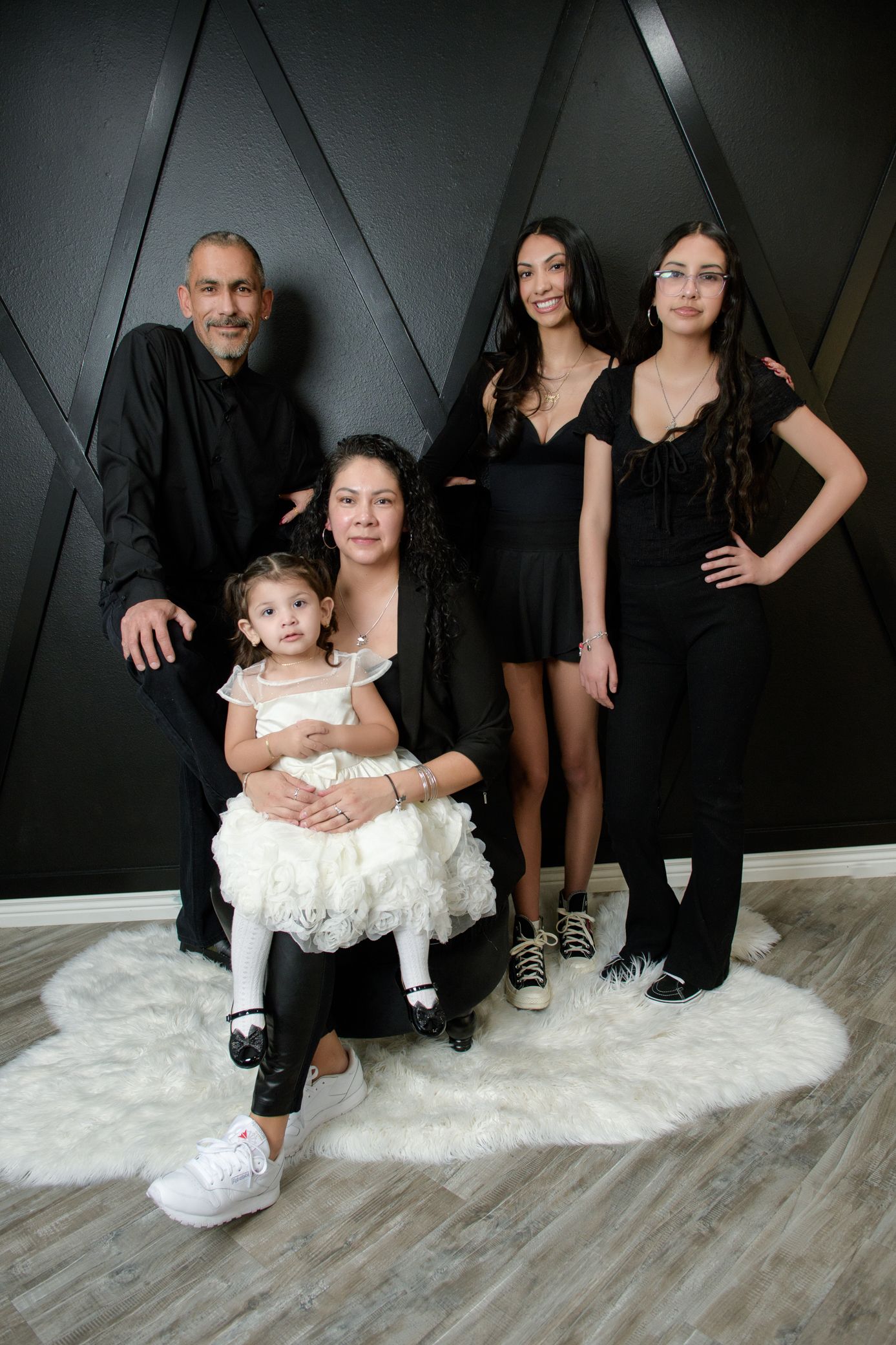 Family of five posing for a portrait against a black geometric wall, dressed in black and white outfits.