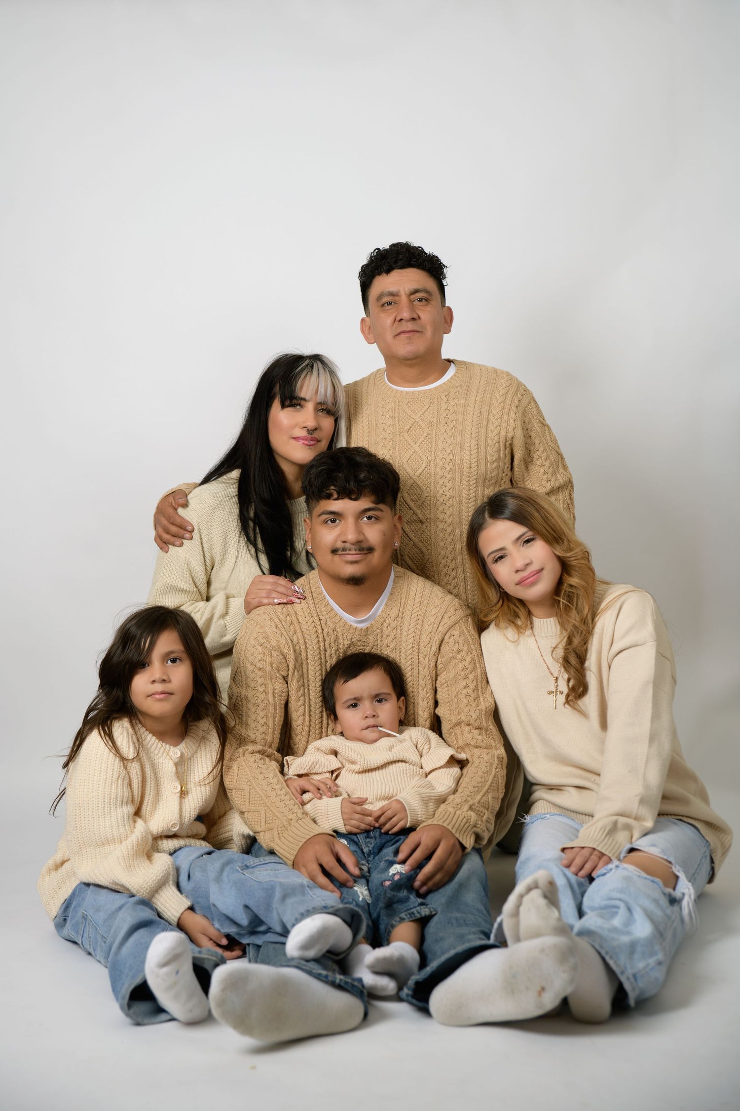 Family of six in matching cream cable-knit sweaters and jeans posing together for a studio portrait on white background.