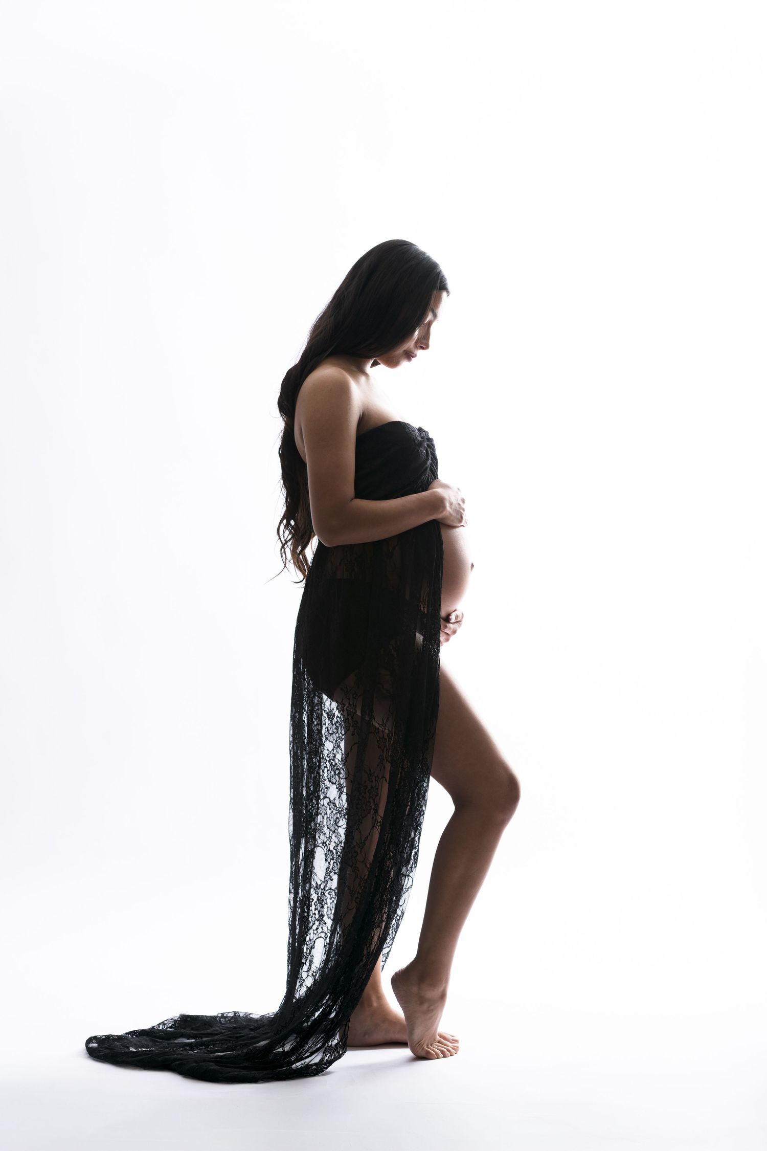 Pregnant woman in black lace dress cradling baby bump, silhouette against white background, maternity photography.