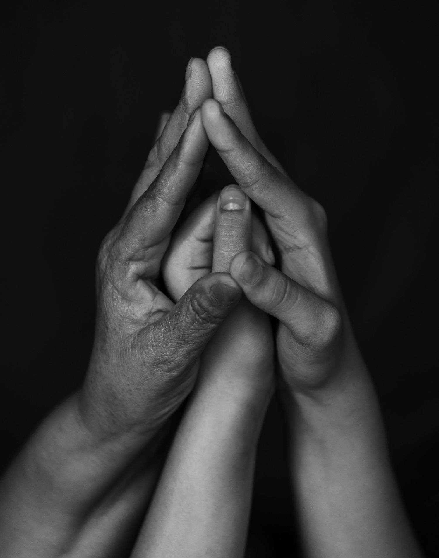 Black and white photo of elderly and young hands pressed together in prayer gesture.