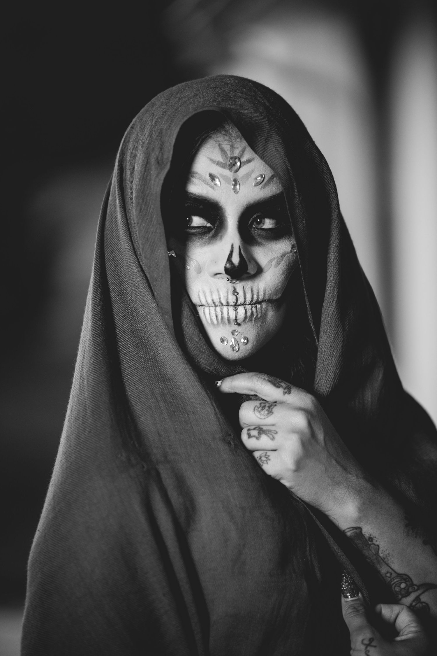 Black and white portrait of woman in hooded veil with detailed sugar skull face paint.