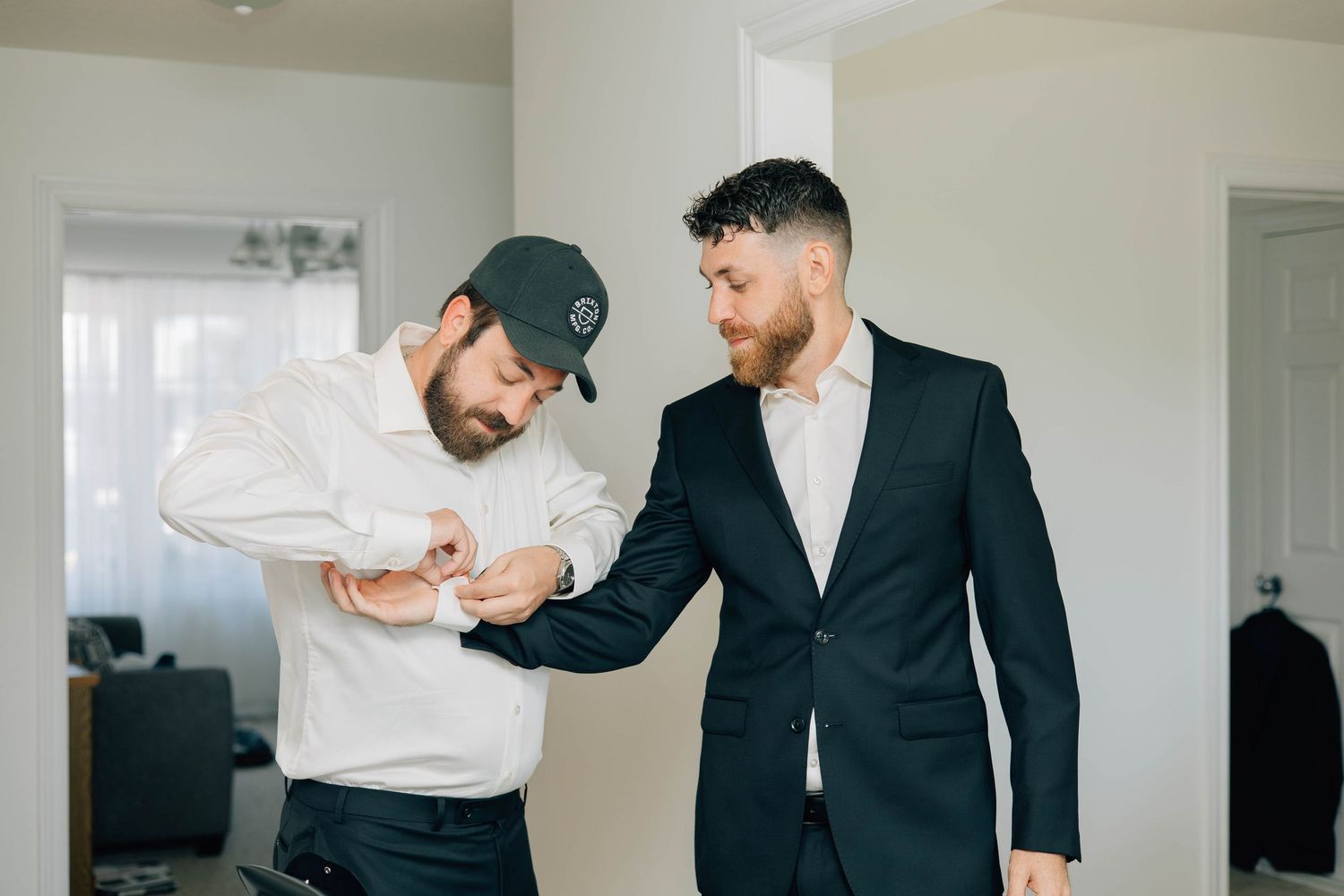 Groomsman helping groom adjust his suit cufflinks while getting ready for wedding.