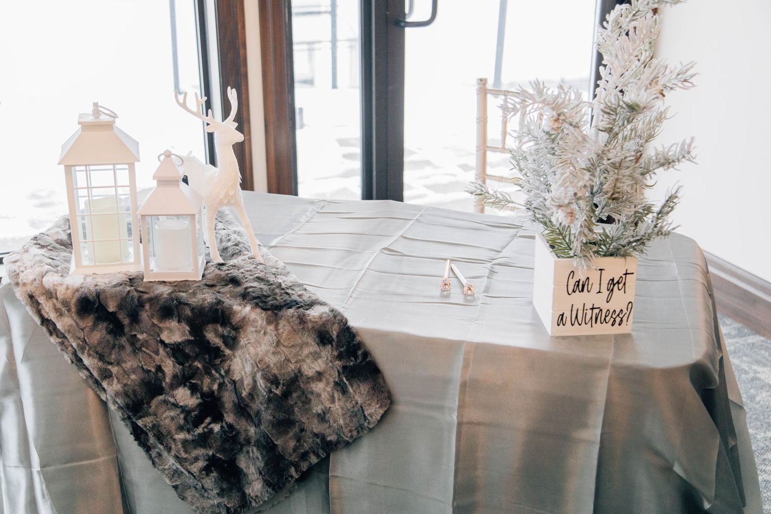 Winter wedding wish table with white lantern, deer figurine, snowy tree, and a can I get a witness sign.