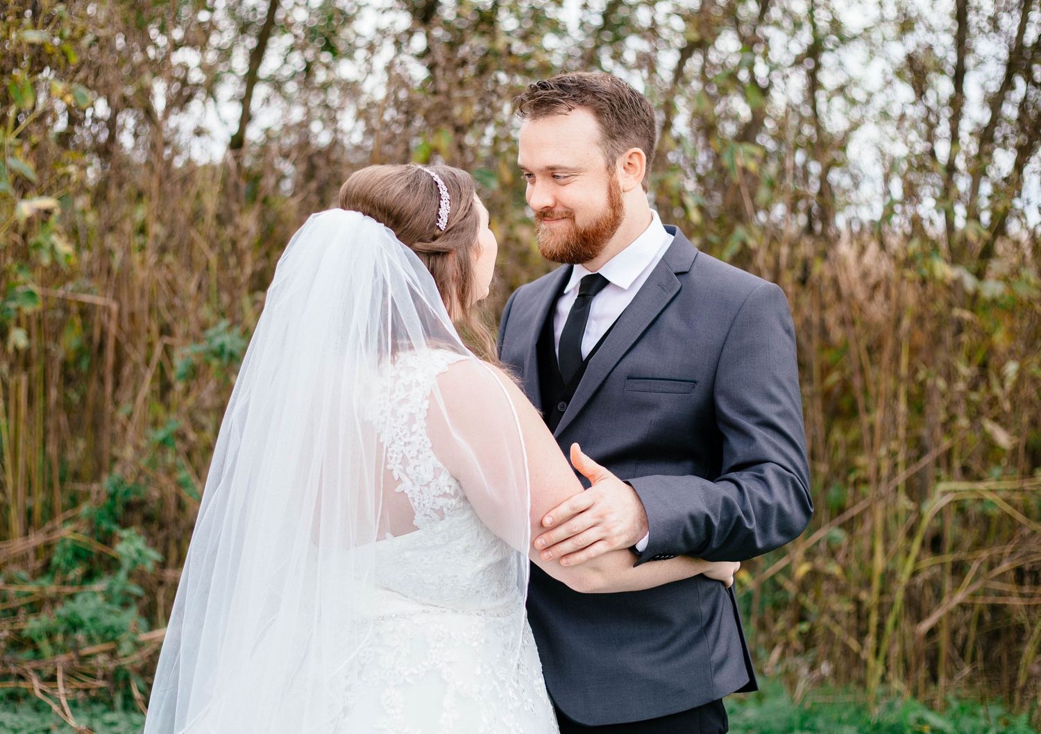 Groom smiling warmly at bride in lace wedding gown during intimate outdoor first look.
