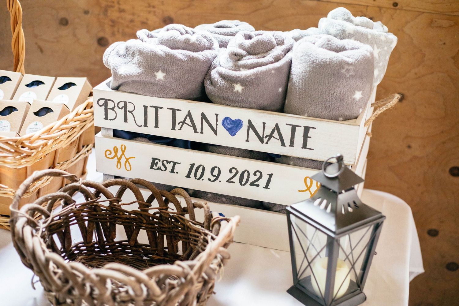 Wedding keepsake crate reading Brittan and Nate Est. 10.9.2021 with rolled gray blankets and wicker basket.