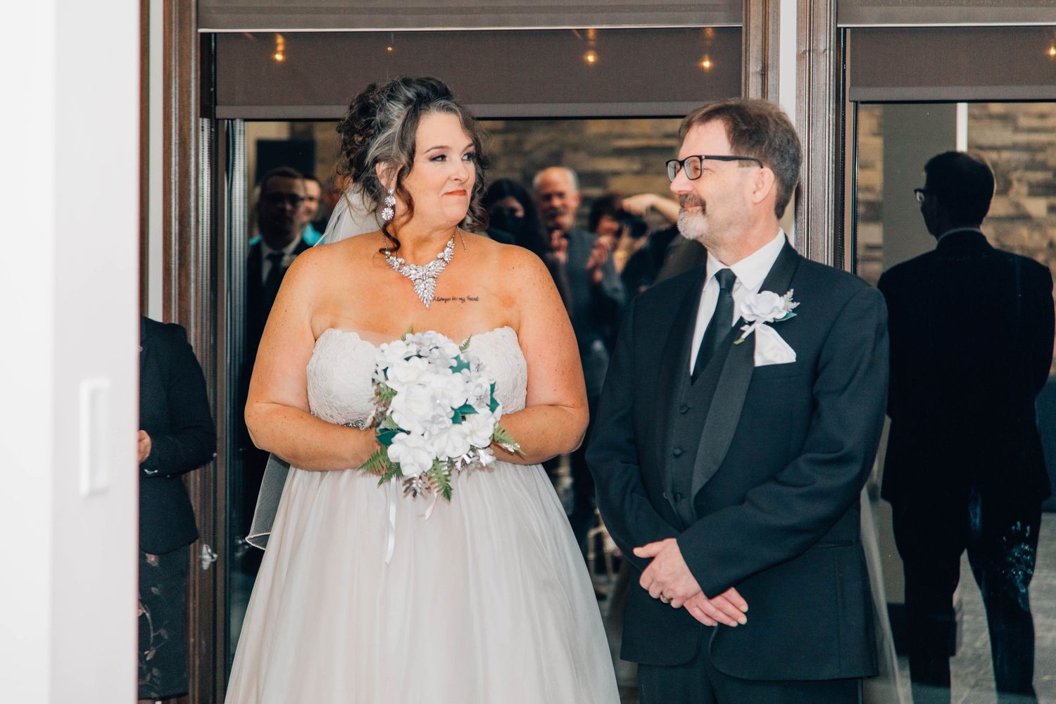 Bride in ballgown holding white bouquet walks with groom in black tuxedo at wedding venue entrance.