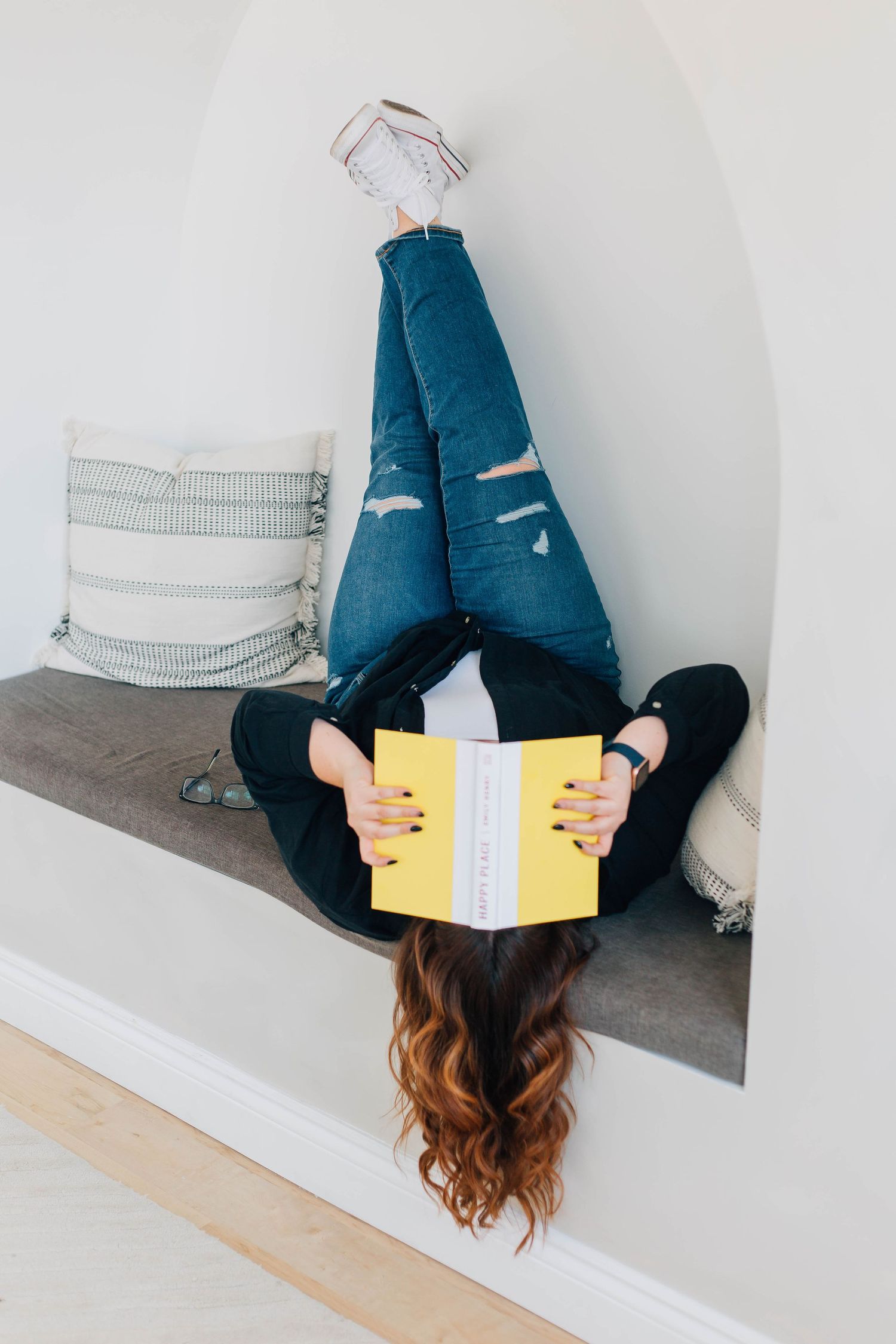Woman lying upside down on bench, covering her face in a book in Kitchener Ontario.