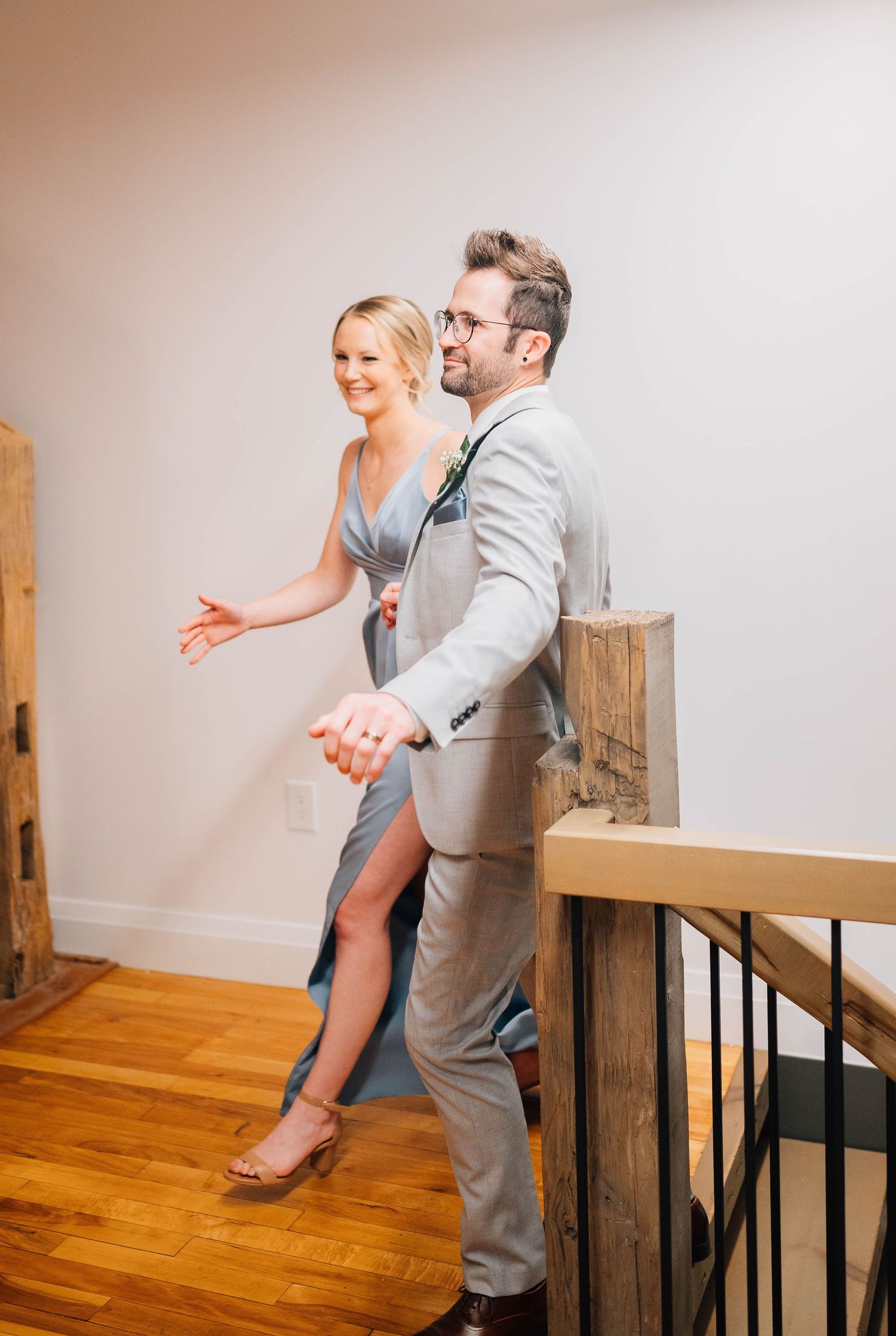 Smiling bridesmaid in blue dress and groomsman in gray suit walking down stairs at wedding reception.