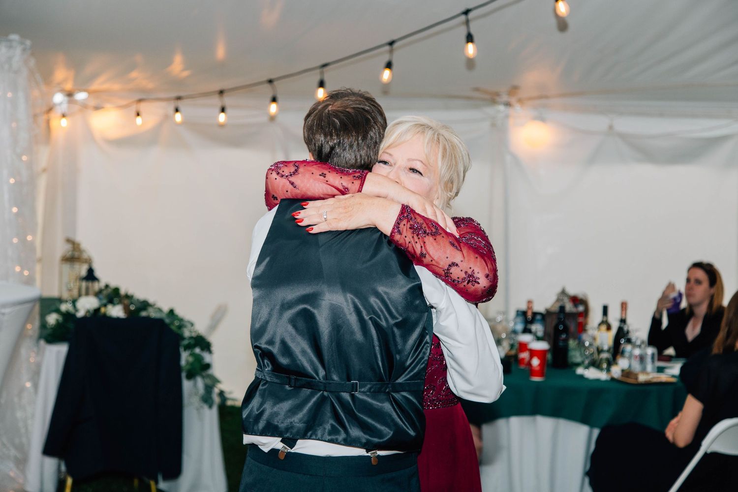 A heartfelt mother-son dance embrace at a wedding reception under warm string lights.