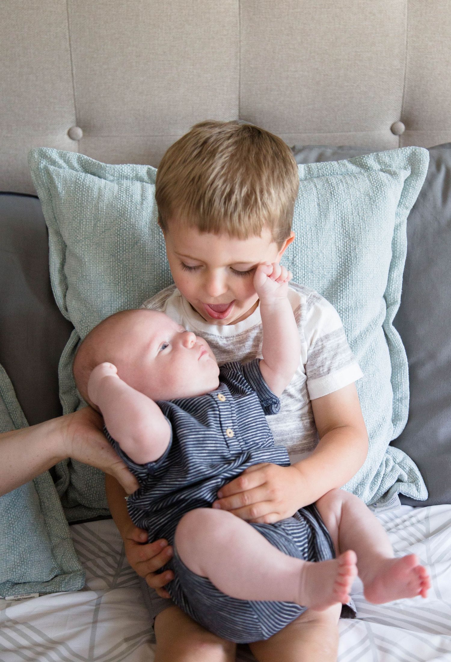 Young boy gently holds his newborn baby sibling on a bed with pillows.